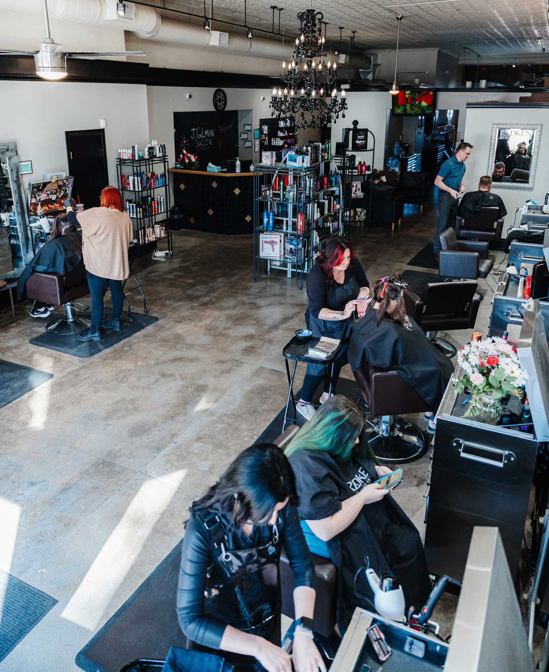 A busy hair salon with stylists working on clients and shelves filled with various hair products.